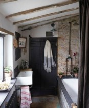 a barn bathroom with a brick wall, wooden beams on the ceiling, dark furniture and a window to brign natural light in