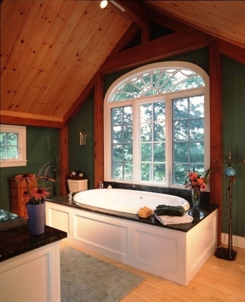 a barn bathroom with a wooden plank ceiling, wooden beams, a raised bathtub and green walls