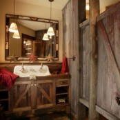 a rustic bathroom clad with reclaimed wood, with a vintage mirror, a reclaimed wooden vanity and bright towels