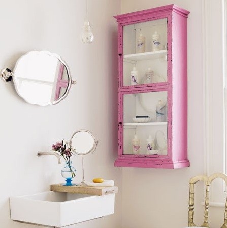 A chic guest toilet with a pink storage unit, a wall mounted sink and some mirrors
