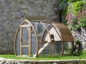 a boat-shaped catio of wood and mesh, with green lawn, a house and a ladder is a simple and natural space to stay