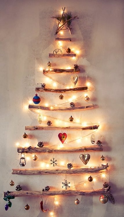 A wall mounted Christmas tree of sticks with lights and various ornaments for a Nordic feel in the space