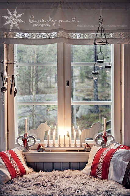 red and white linens, faux fur, a white curtain with Nordic decor and a candleholder with severla candles plus wooden horses