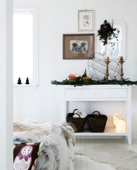 evergreens, baskets, candles in wooden candleholders, a bowl with metallic ornaments and greenery