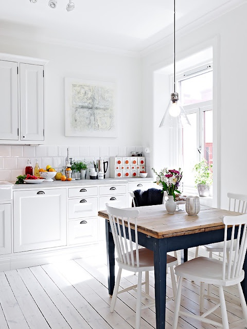 a pure white Scandinavian kitchen with retro cabinets, a glass pendant lamp and a vintage navy dining table