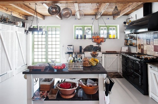 a cozy white Scandi kitchen with a large blakc cooker and hood, with a black and white kitchen island and a wooden ceiling with beams and cookware