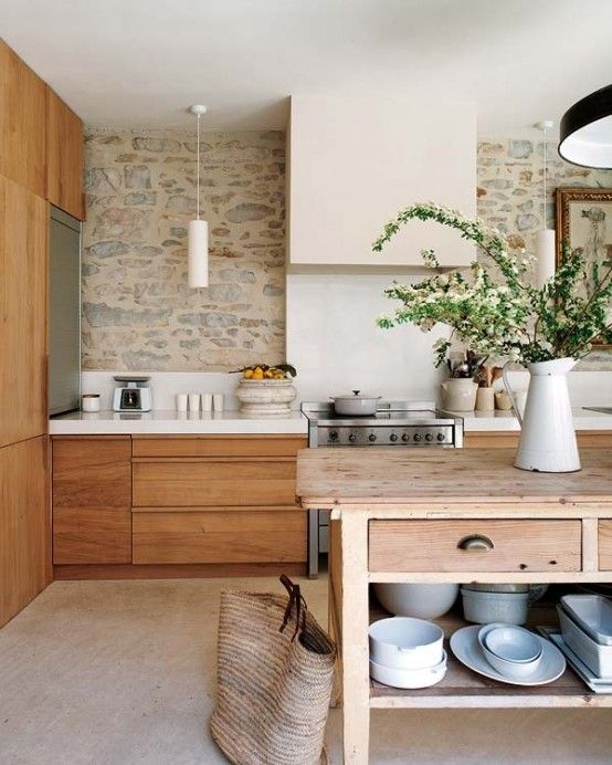 a welcoming earthy tone kitchen with  a stone wall, warm-stained furniture, a wooden kitchen island and pendant lamps