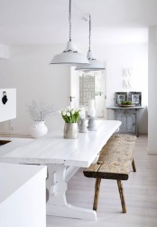a pure white Scandinavian kitchen with a white rustic table, a rough wooden bench and a light blue cabinet with photos