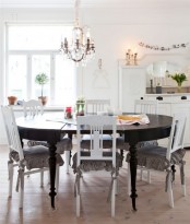 a vintage Scandinavian kitchen with white cabinets, a crystal chandelier, a black round table and white vintage chairs