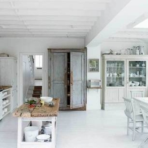 A white Nordic kitchen with an off white buffet, a white dining set, a shabby chic cupboard and a rustic kitchen island