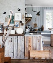 a cozy rustic kitchen with light blue shiplap on the walls, rough wood cabinets, branches and wall lamps