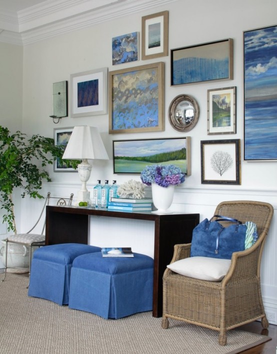 a dark console, a large gallery wall with seascapes, a rattan chair and touches of bright blue