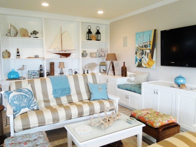 A neutral beachy living room with a striped sofa, a built in shelving units with items on display and some sea inspired accessories