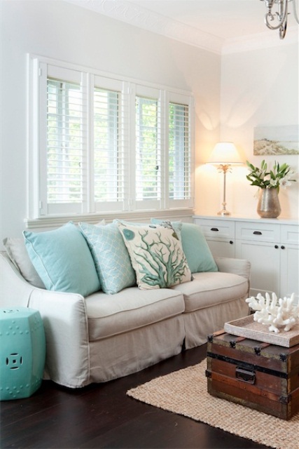 a small white beach living room with touches of turquoise, a stained chest for storage and an artwork