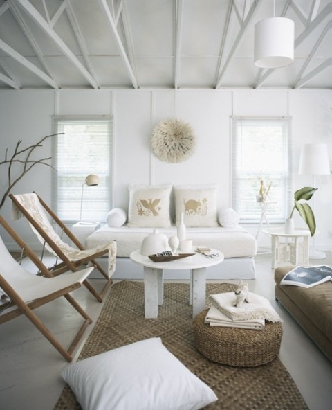 a relaxed white living room with jute ottomans and rugs, folding beach chairs, printed pillows