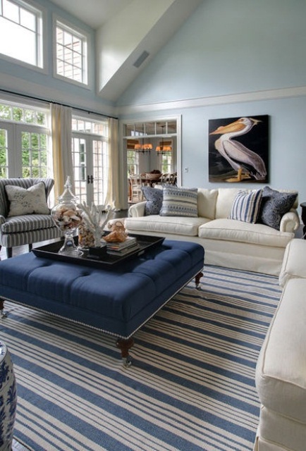 A blue and navy beach living room with stripes, a pelican artwork and much sea inspired decor on the ottoman