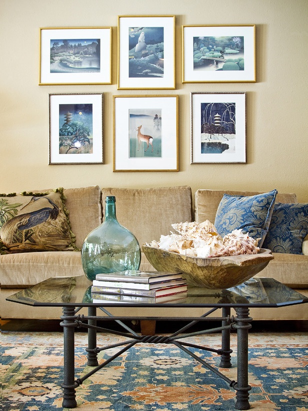 A modern beach living room with sandy walls, a gallery wall with sea inspired artworks, a glass table and a tan sofa