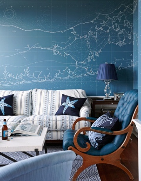 A sea inspired living room with an accent map blue wall, a matching chair,  a striped sofa and navy lamps