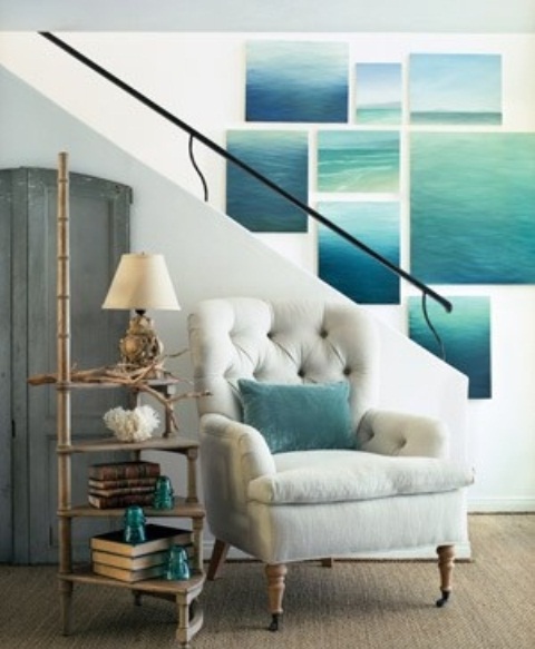A bold and large sea inspired gallery wall, a white upholstered chair and an etagere with books and aqua accessories