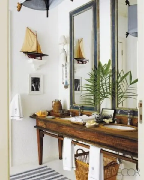 a nautical bathroom with a vintage wooden vanity, teal frame mirrors, a ship decoration and a basket for storage