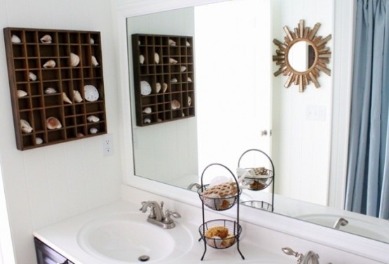 a neutral bathroom with a box shelf with seashells and starfish, a sunburst mirror and a stand with soaps and sponges