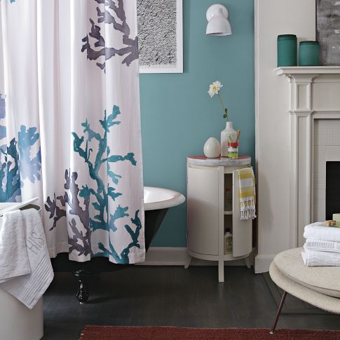 a blue bathroom with a dark floor, a coral print shower curtain, a white table with storage