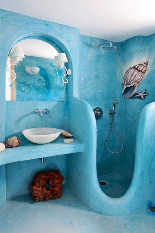 a blue painted plaster bathroom with a carved shower space, lamps, stones, corals and a painted seashell