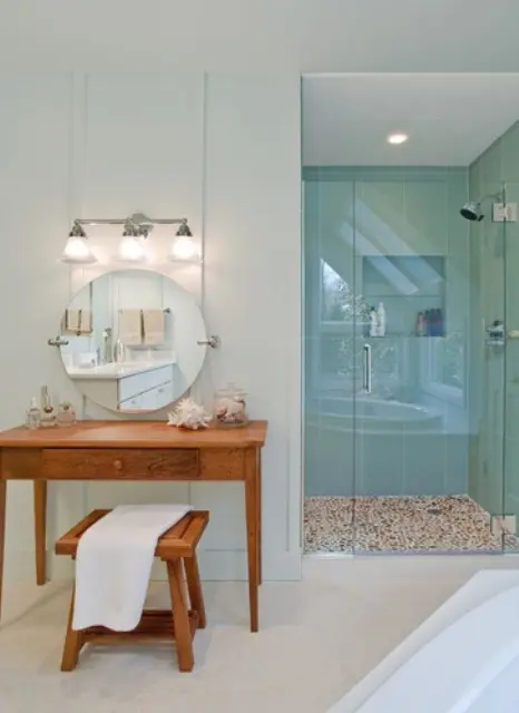 a neutral beachy bathroom with aqua-colored tiles in the shower, a wooden vanity plus a stool and some sea creatures 