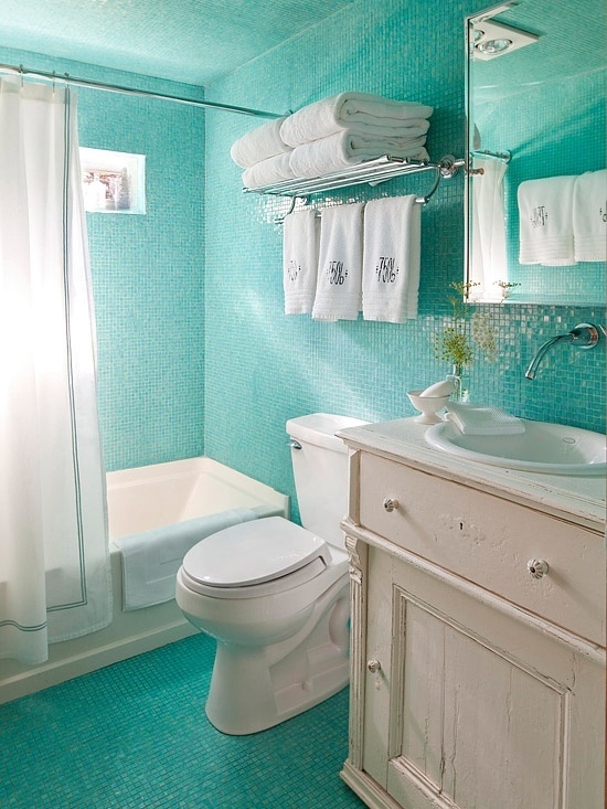 a bright turquoise bathroom with white touches, creamy furniture, towels and a shower curtain