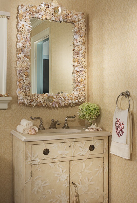 a neutral sink space with a textural vanity, a seashell and starfish clad mirror, coral printed towels