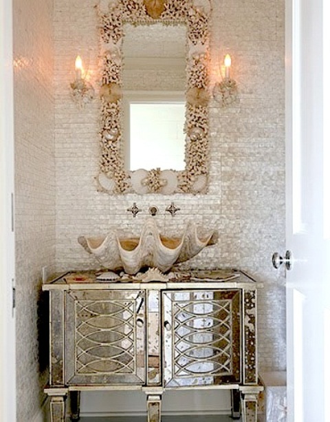 a neutral bathroom with a shiny glam vanity, a starfish and seashell framed mirror and a giant shell sink