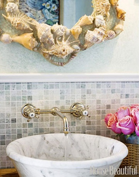 a marble sink and a mirror clad with seashells and starfish for a sea inspired bathroom