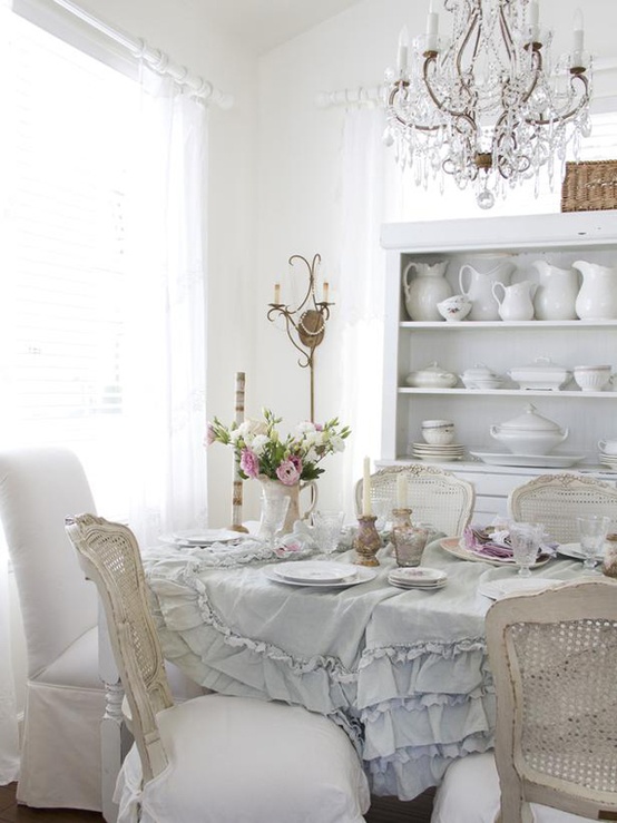 an elegant and neutral shabby chic dining room with a ruffle tablecloth, a crystal chandelier, shabby chic chairs and stylish porcelain