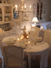 a white shabby chic dining room with elegant furniture, a crystal chandelier, some porcelain and glass and a cool lamp