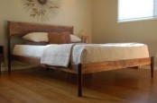 a simple and elegant stained wooden bed with a headboard and tall legs is cool and chic