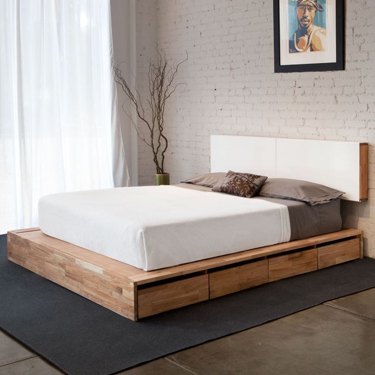 A light stained platform mid century modern bed with drawers and a minimal white headboard attached to the wall