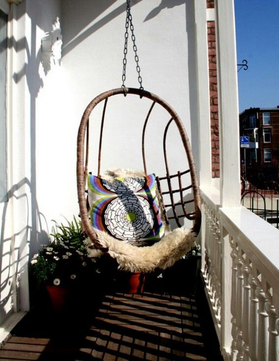 A small balcony with a suspended egg shaped chair, potted plants and pillows is a welcoming nook to spend some time