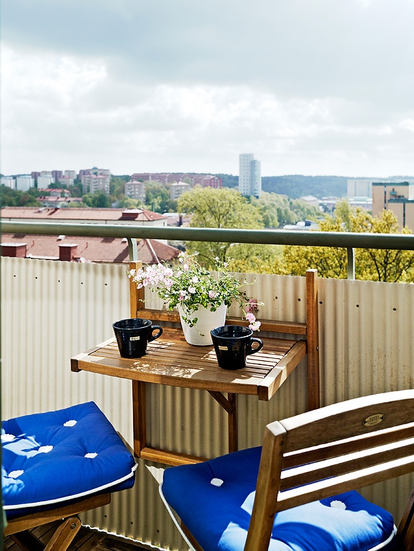 A small balcony with greenery, a folding table and chairs, bright cushions, is a great and cool space to be in