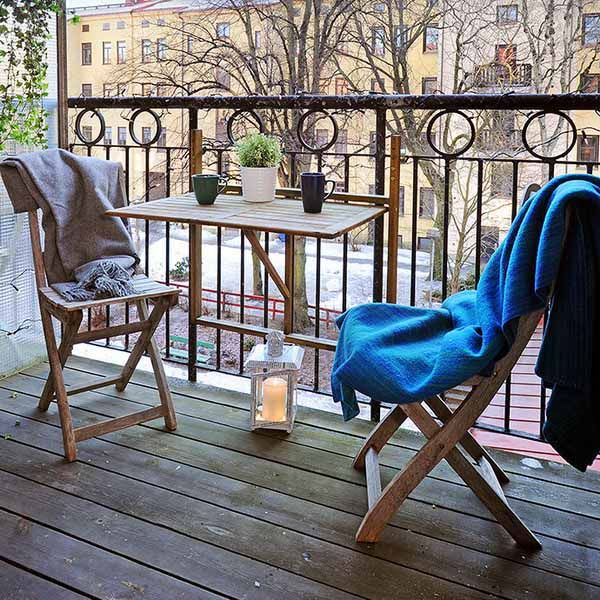 A small balcony with folding furniture   a table and chairs, a candle lantern and blankets to cozy up the space