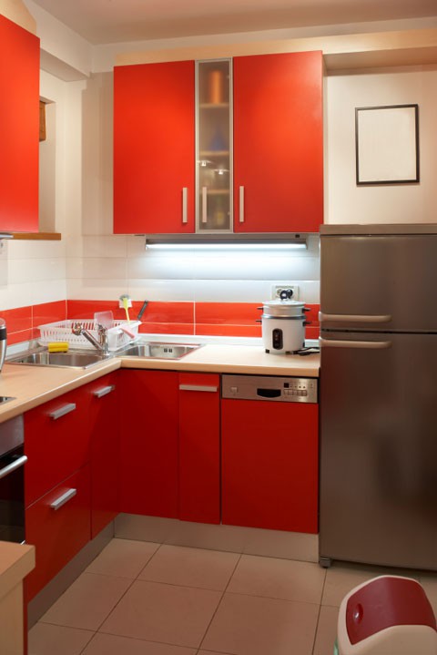 a bright kitchen with red cabinetry and a bold tile backsplash, neutral tiles and a stainless steel fridge