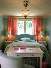 a mint green bedroom done with a matching bed, green and white bedding, coral printed curtains, a white desk and a mint chair