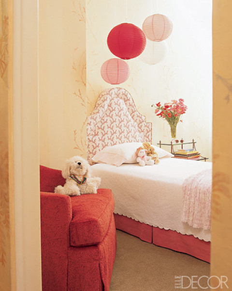 a small and lovely kid's room with a red bed with neutral bedding, a red basket with toys, paper lamps in matching colors