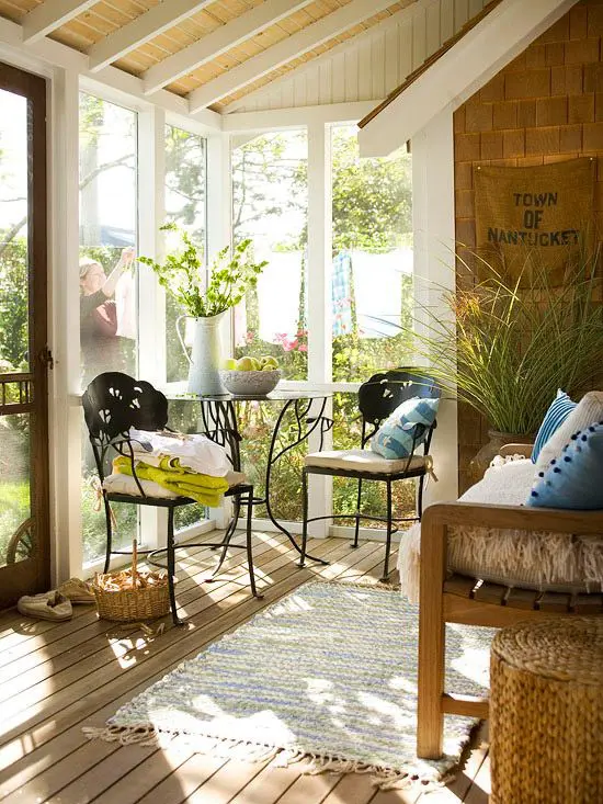 a chic eclectic sunroom space with forged chairs and a table and a wooden benches with textiles and accessories