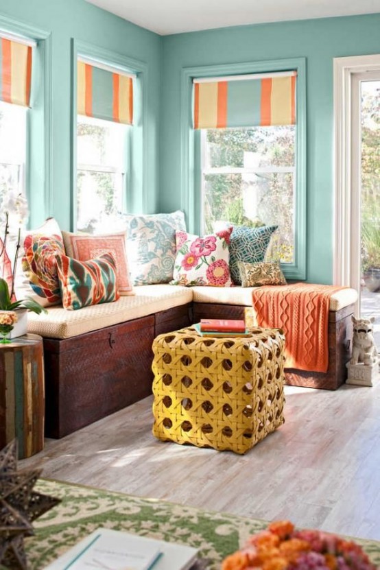 a small and colorful sunroom with turquoise walls, colorful and printed details and a wicker ottoman