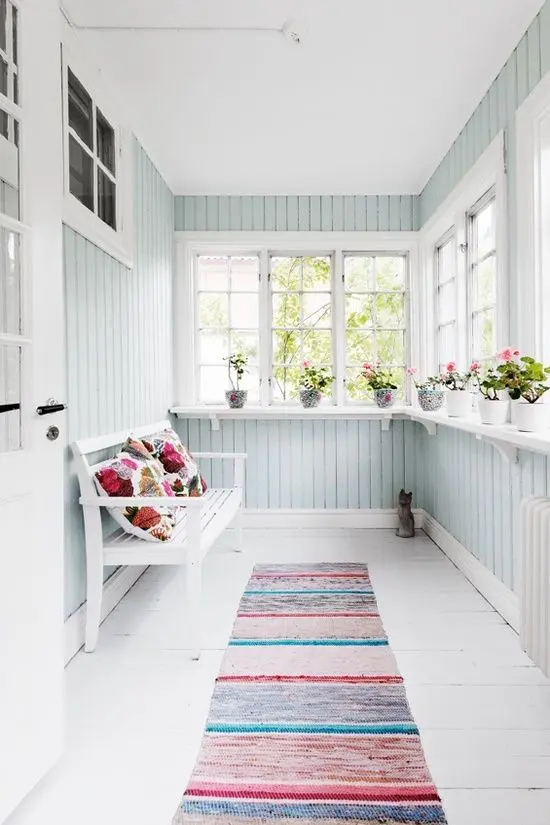 a small pastel sunroom in a light aqua shade, colorful textiles and a bench plus potted blooms