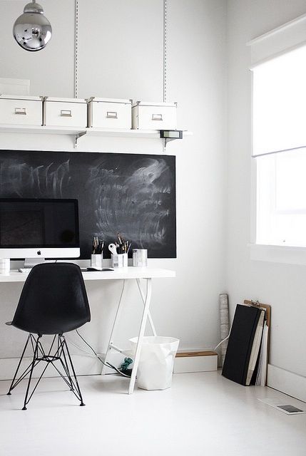 a white home office with a white desk and a black chair, a chalkboard for chalking plans and boxes on a shelf is a lovely space to work in