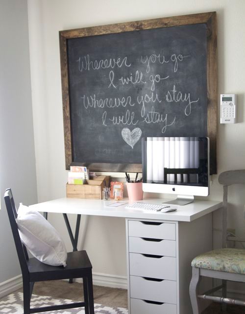 a small rustic working space with a white desk, a dark chair, a large chalkboard in a frame, a PC and an additional vintage chair