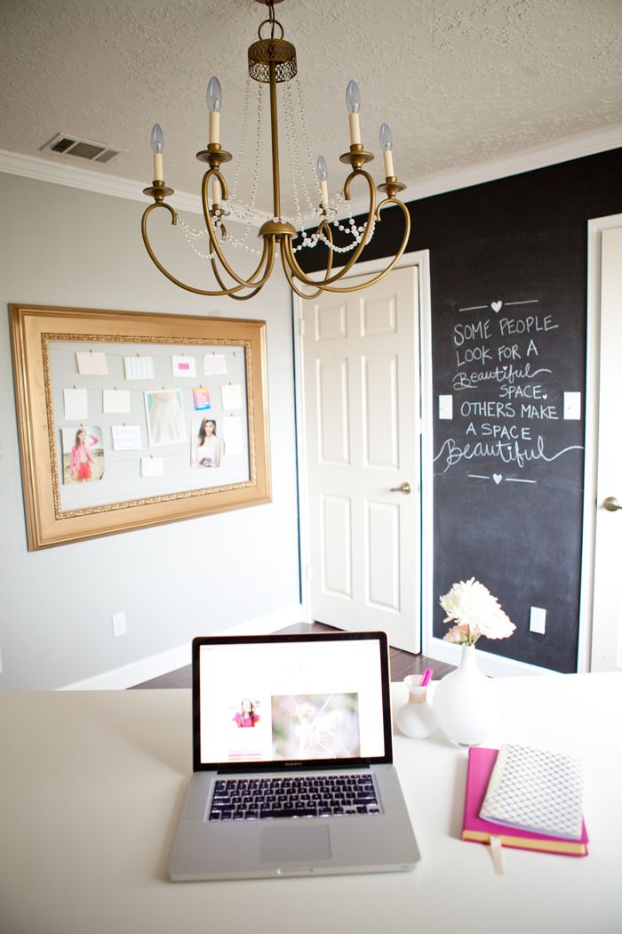 A vintage home office with a chalkboard accent wall for making notes, a white desk, a large board with memos and a vintage chandelier
