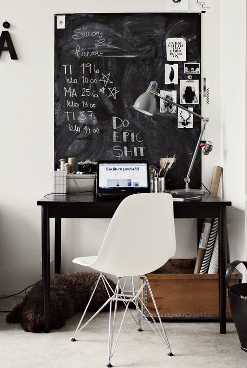 a mini working nook with a large chalkboard for leaving notes, a small black desk and a white chair, a box with various stuff