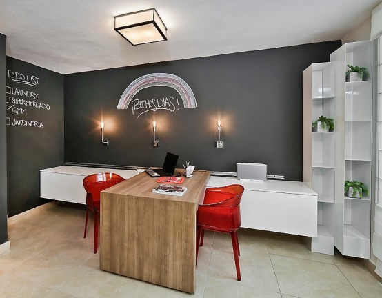 a modern shared home office with a chalkboard accent wall for leaving notes and marks, a white floating storage unit, a stained desk and red chairs